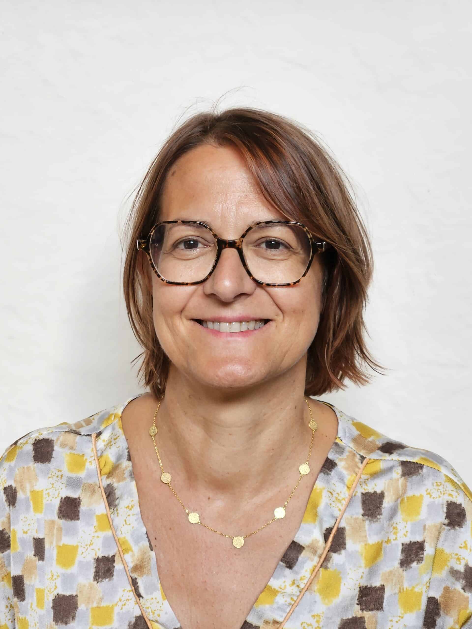 Photo de Frédérique Capelle, consultante juriste en marchés publics. Portrait professionnel avec un fond neutre, vêtue d'une blouse à motifs discrets et d'un collier doré, incarnant expertise et professionnalisme.